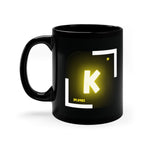 A black coffee mug with a white and yellow logo on the side. The logo features the chemical symbol for potassium (K)